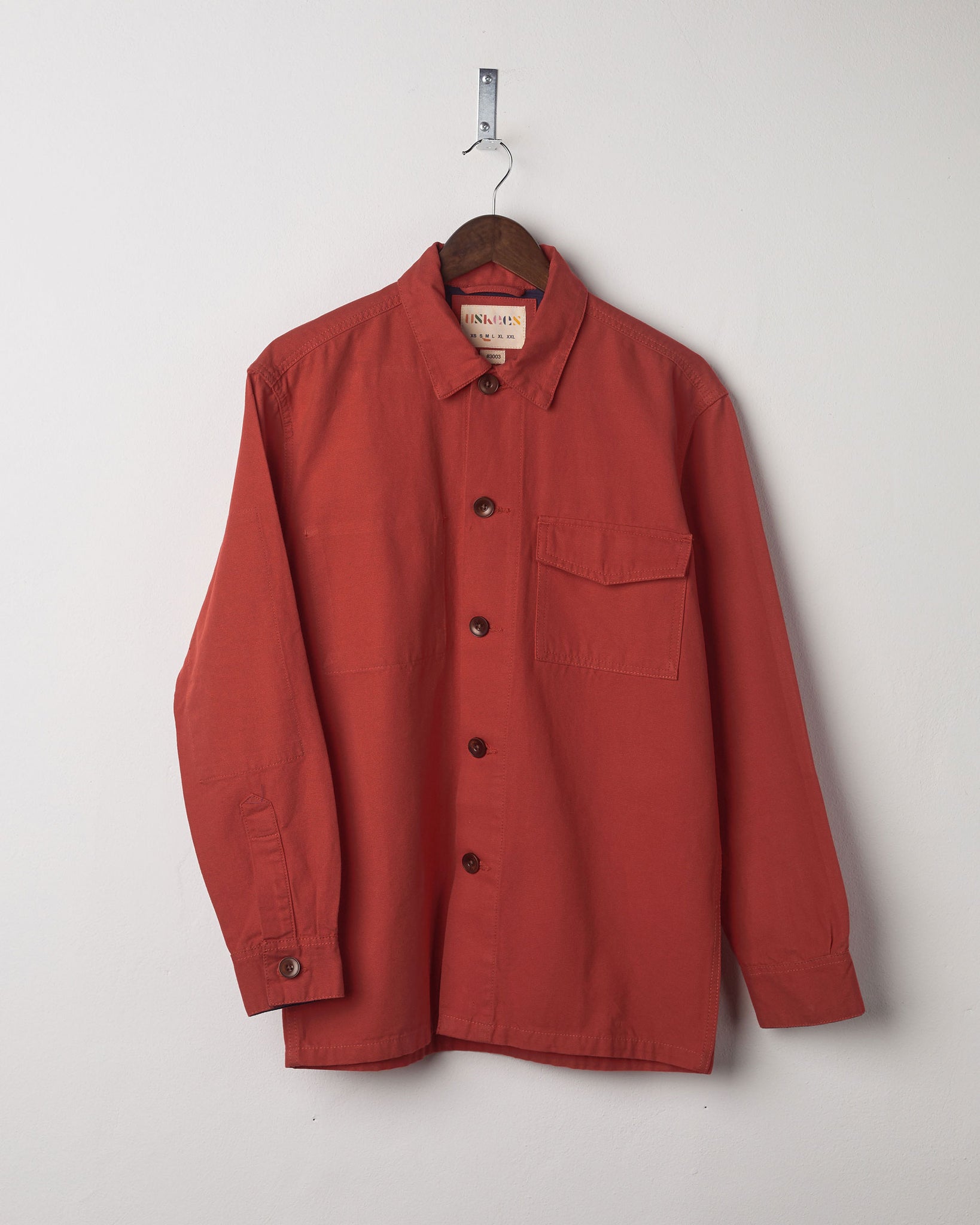 Front view of the terracotta-red buttoned 3003 workshirt from Uskees presented on hanger.