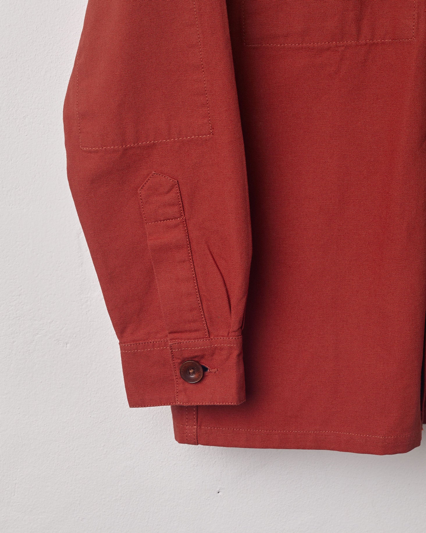 View of the mid-section and sleeve of the #3003 Uskees button-down work shirt in terracotta-red with focus on cuff, placket and corozo buttons.