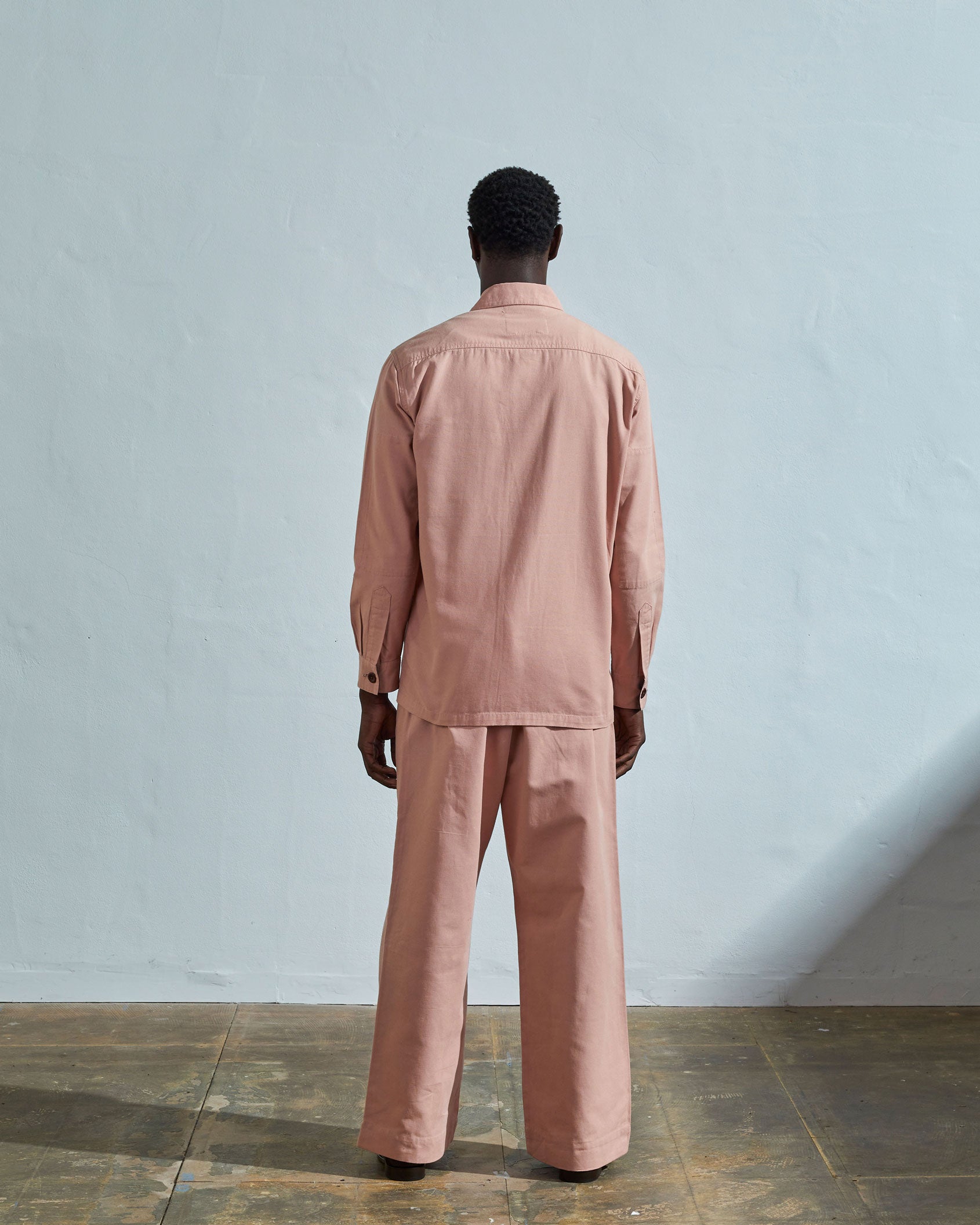 Back view of model wearing Uskees #3003 men's dusty pink workshirt showing reinforced elbow area and corozo buttoned cuffs.