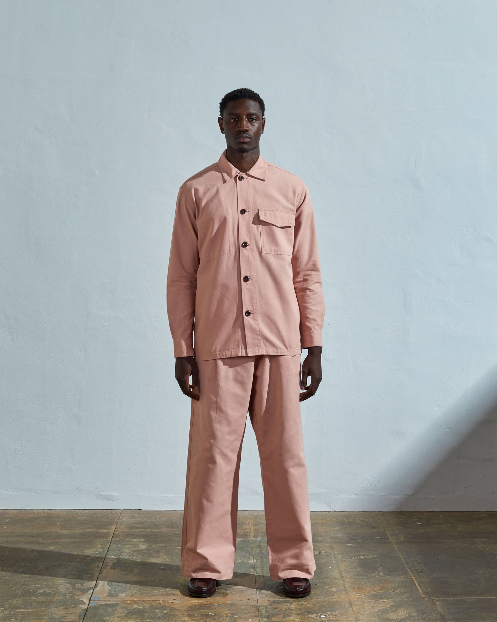 Full-length view of model wearing Uskees #3003 dusty pink workshirt illustrating utilitarian silhouette. Paired with Uskees matching pants.