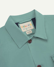 Close-up top-half view of #3003, eucalyptus (mint-green) organic cotton workshirt. With focus on collar, Uskees brand label and corozo buttons.