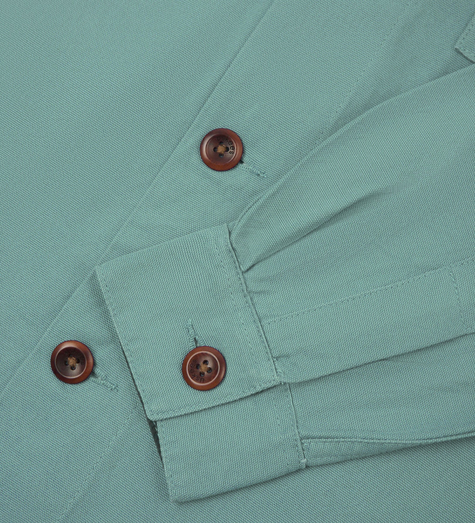 View of the mid-section and sleeve of the 3003 Uskees button-down work shirt in eucalyptus with focus on cuff, placket and corozo buttons.
