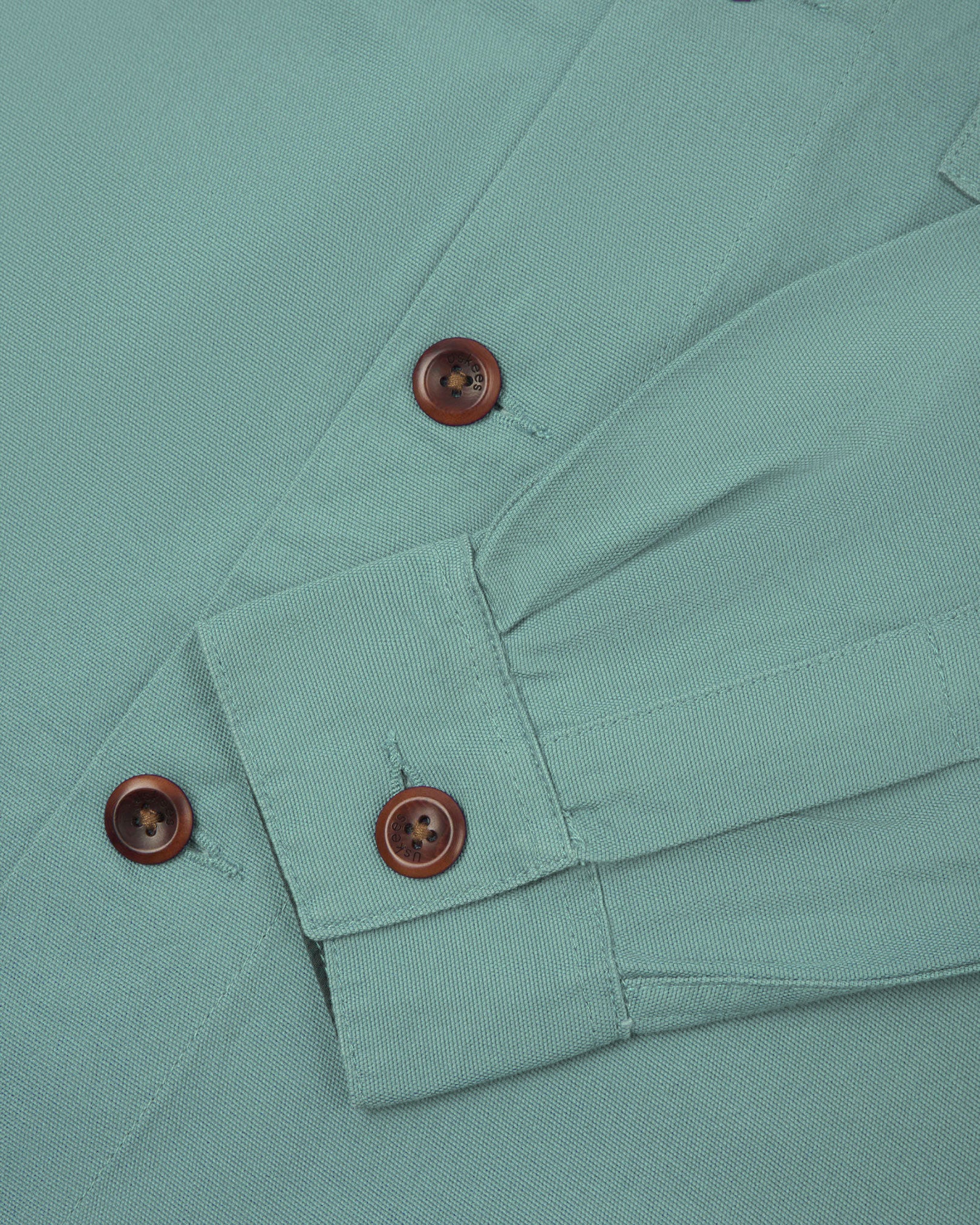 View of the mid-section and sleeve of the 3003 Uskees button-down work shirt in eucalyptus with focus on cuff, placket and corozo buttons.