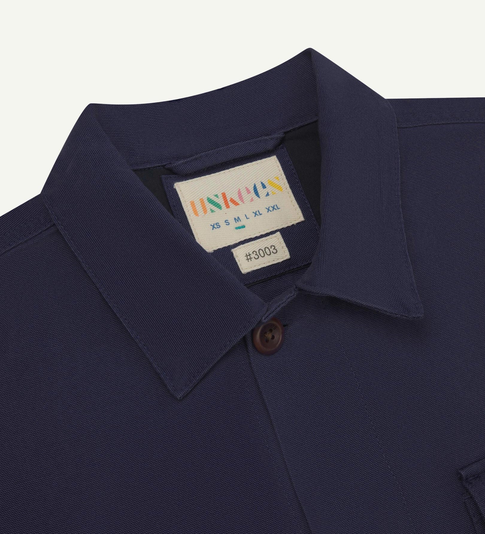 Close-up top-half view of #3003, midnight blue organic cotton workshirt. With focus on collar, Uskees brand label and corozo buttons.