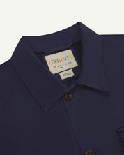 Close-up top-half view of #3003, midnight blue organic cotton workshirt. With focus on collar, Uskees brand label and corozo buttons.