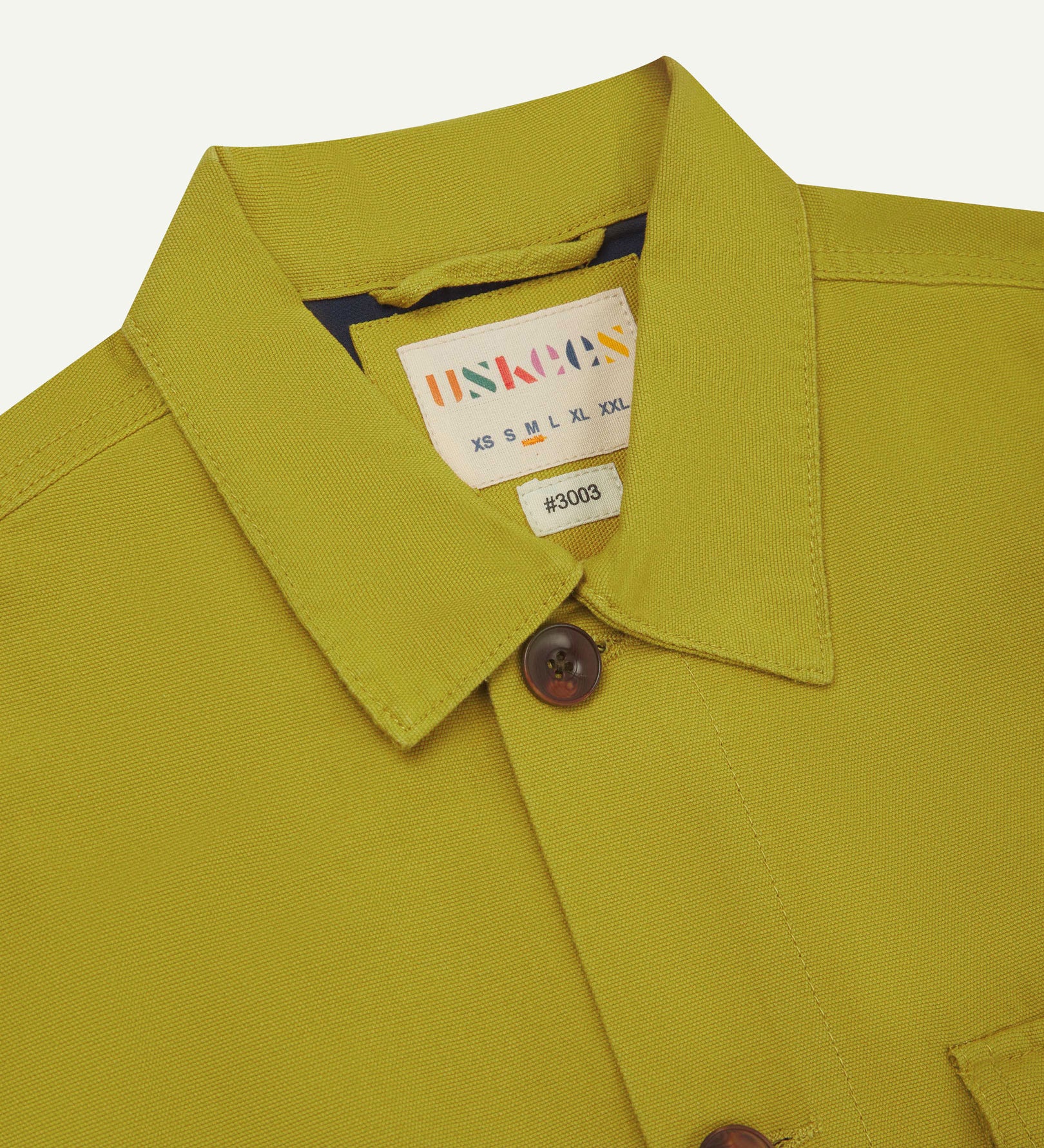 Close-up top-half view of #3003, yellow-green (pear)-coloured organic cotton workshirt. With focus on collar, Uskees brand label and corozo buttons.