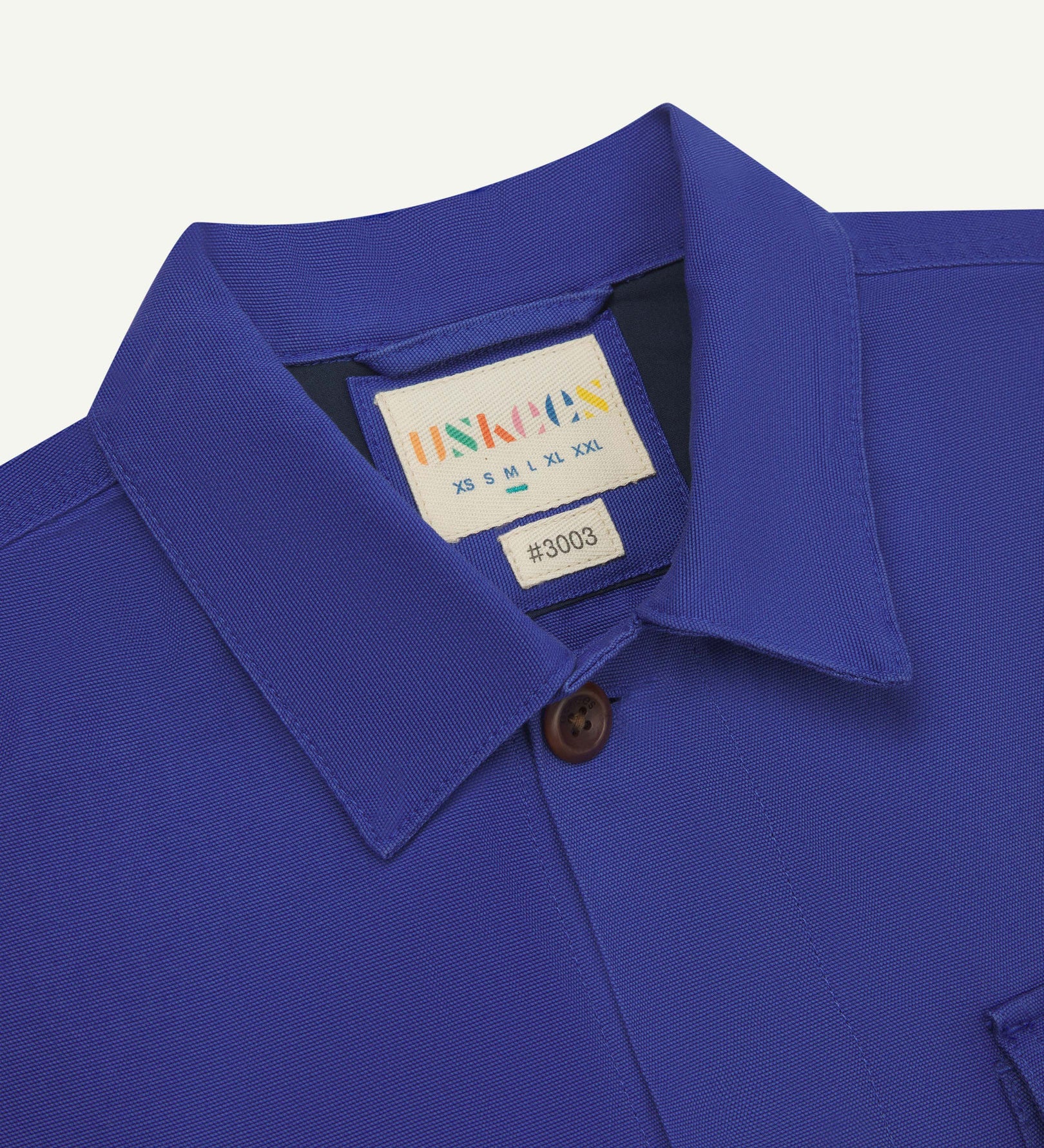 Close-up top-half view of #3003, ultra blue organic cotton workshirt. With focus on collar, Uskees brand label and corozo buttons.