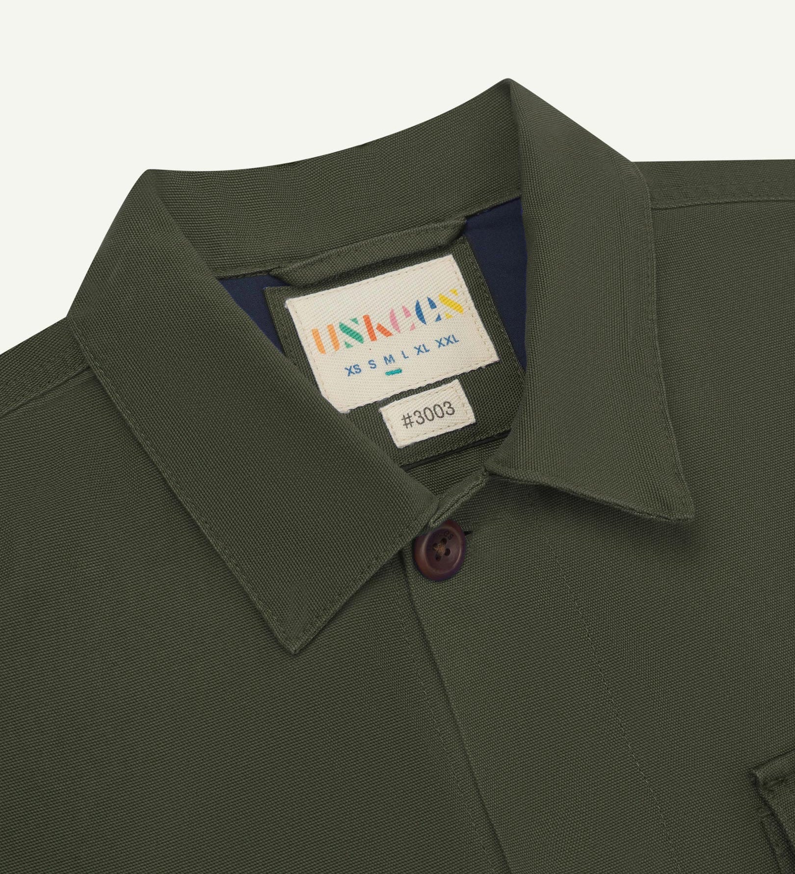Close-up top-half view of #3003, vine green organic cotton workshirt. With focus on collar, Uskees brand label and corozo buttons.