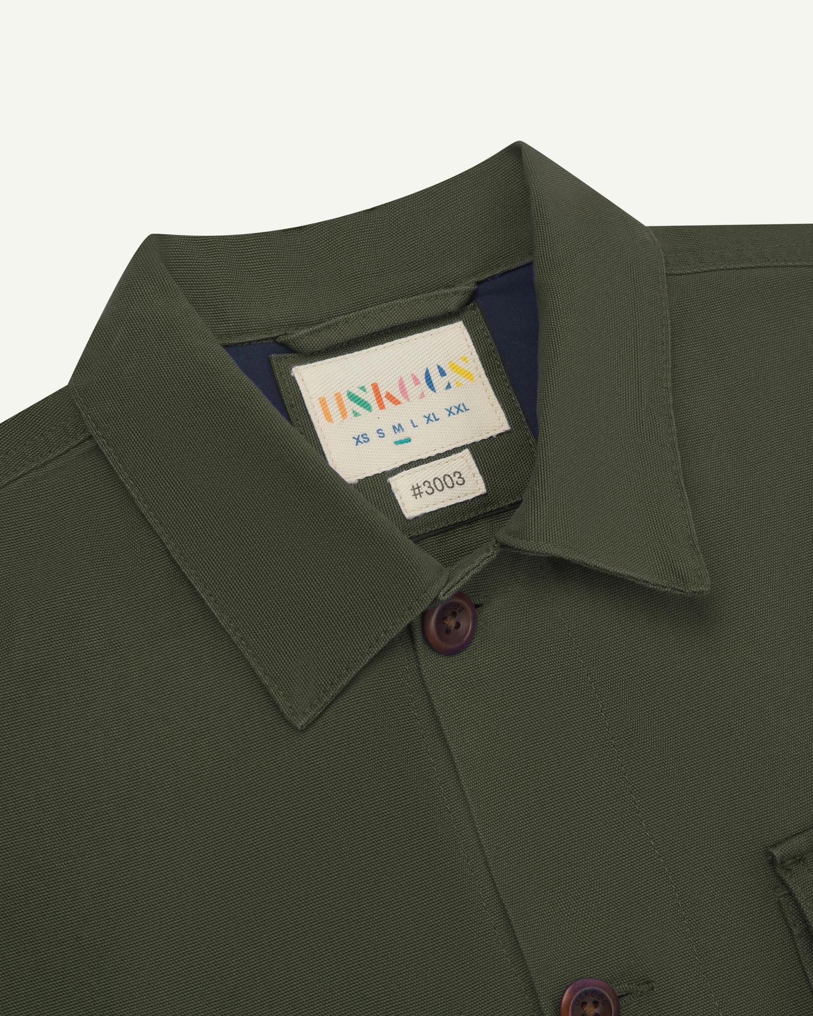 Close-up top-half view of #3003, vine green organic cotton workshirt. With focus on collar, Uskees brand label and corozo buttons.