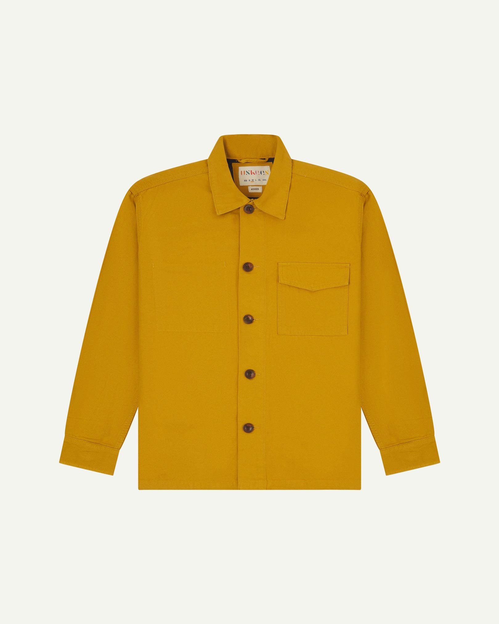 Yellow buttoned organic cotton workshirt from Uskees with clear view of chest pocket and Uskees branding label.