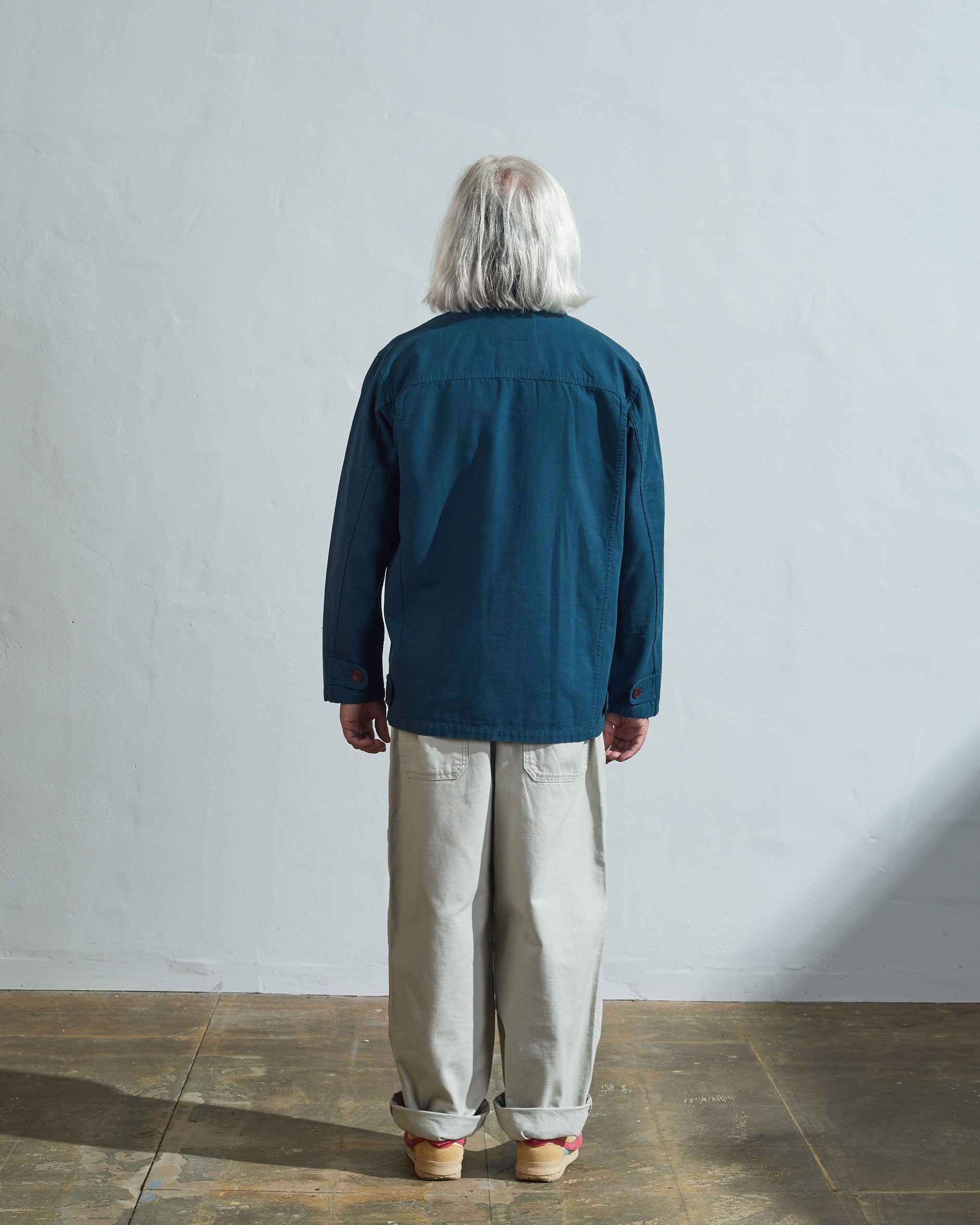 Full-length rear view of model wearing #3004 peacock button-down organic cotton jacket showing reinforced elbows and simple silhouette.