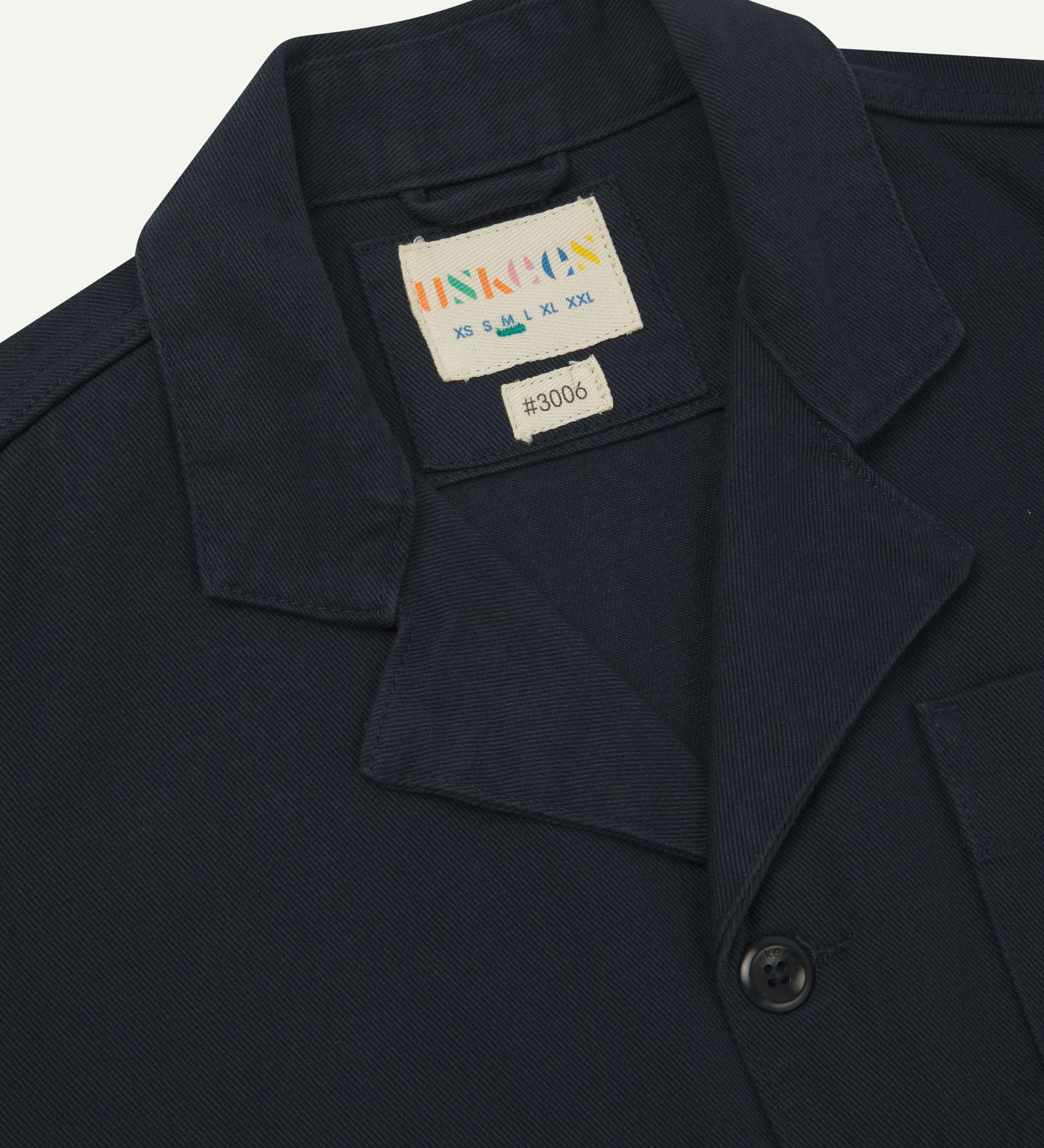 Close-up top-half view of #3006, dark blue (blueberry) organic cotton-drill blazer. With focus on collar, lapels, Uskees brand label and corozo buttons.
