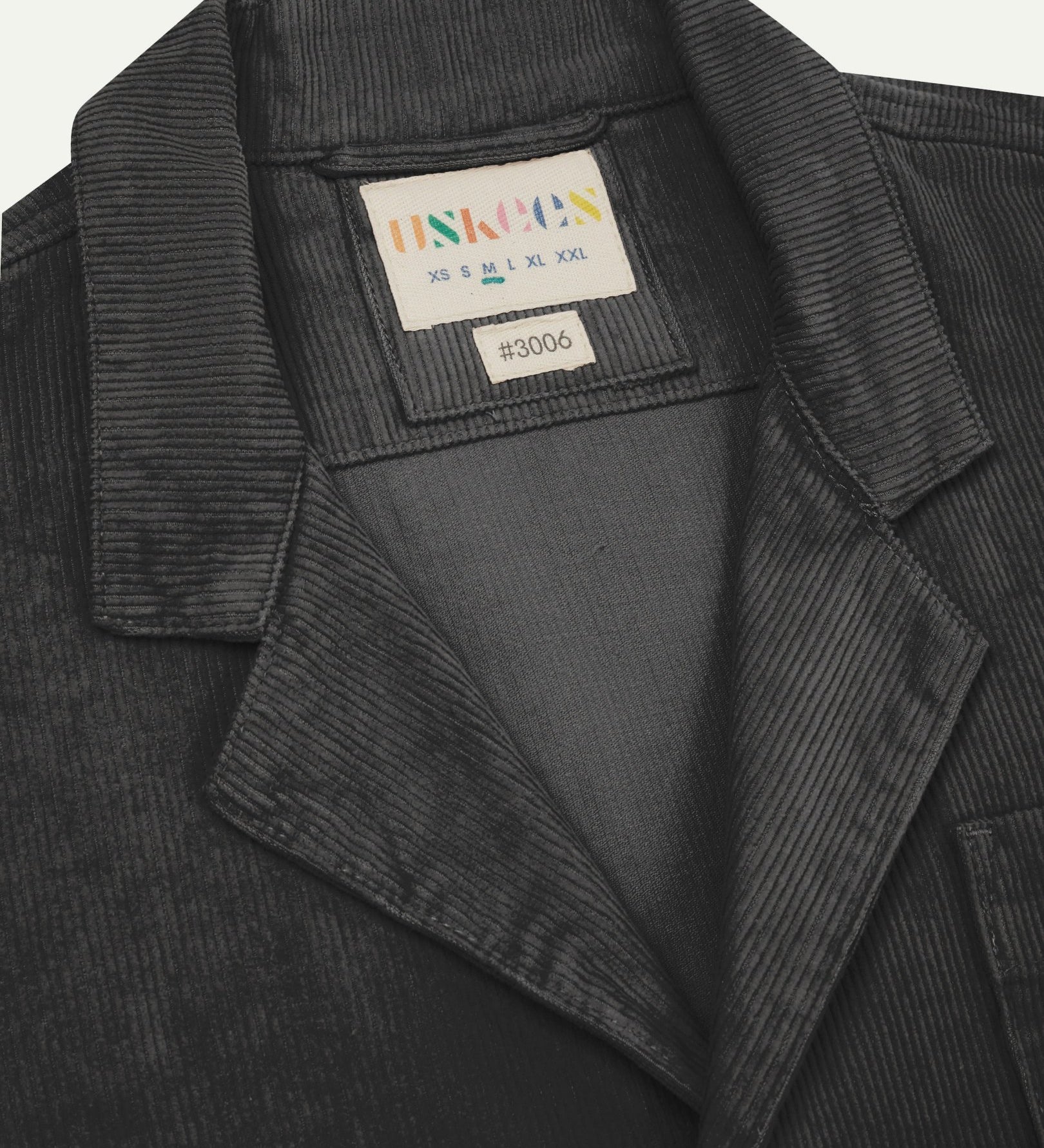 Close-up front view of organic cord charcoal-grey blazer showing the collar, lapels and Uskees brand label.