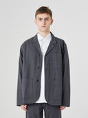 Top-half view of man wearing charcoal-grey buttoned organic cotton-twill blazer. Jacket unbuttoned to reveal white Uskees shirt.
