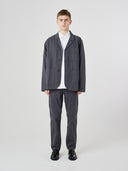 Full-length view of man wearing charcoal-grey buttoned organic cotton-twill blazer with clear view of three patch pockets. Paired with matching Uskees pants.