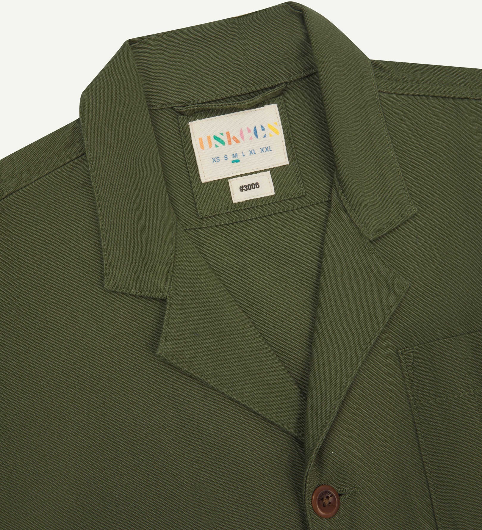 Close-up front view of organic cotton coriander-green blazer showing the collar, lapels and Uskees brand label.
