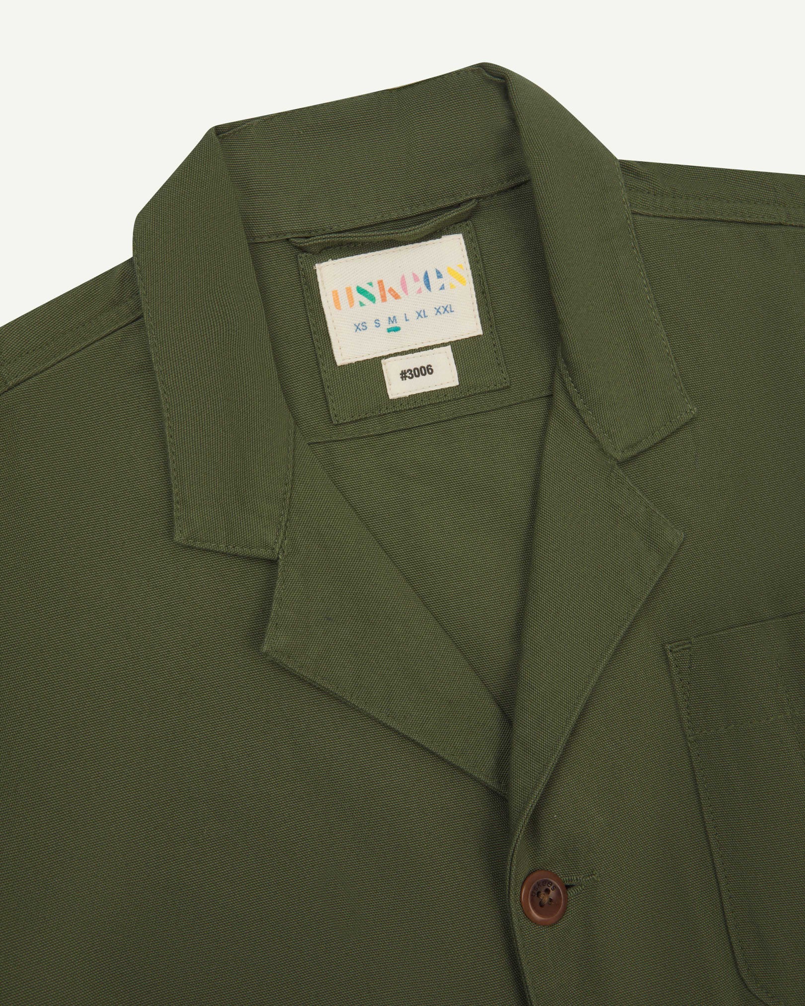 Close-up front view of organic cotton coriander-green blazer showing the collar, lapels and Uskees brand label.