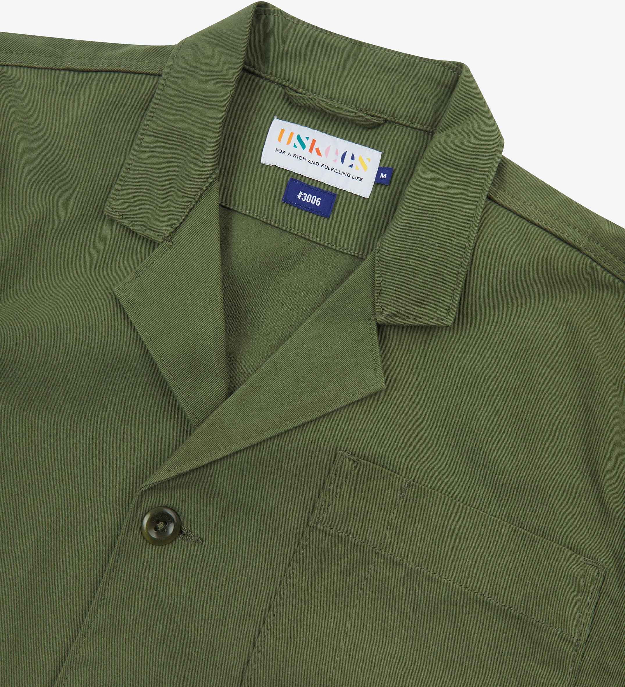Angled top-half view of #3006, coriander-green organic cotton-twill blazer. With focus on collar, lapels, breast pocket, Uskees brand label and corozo buttons.