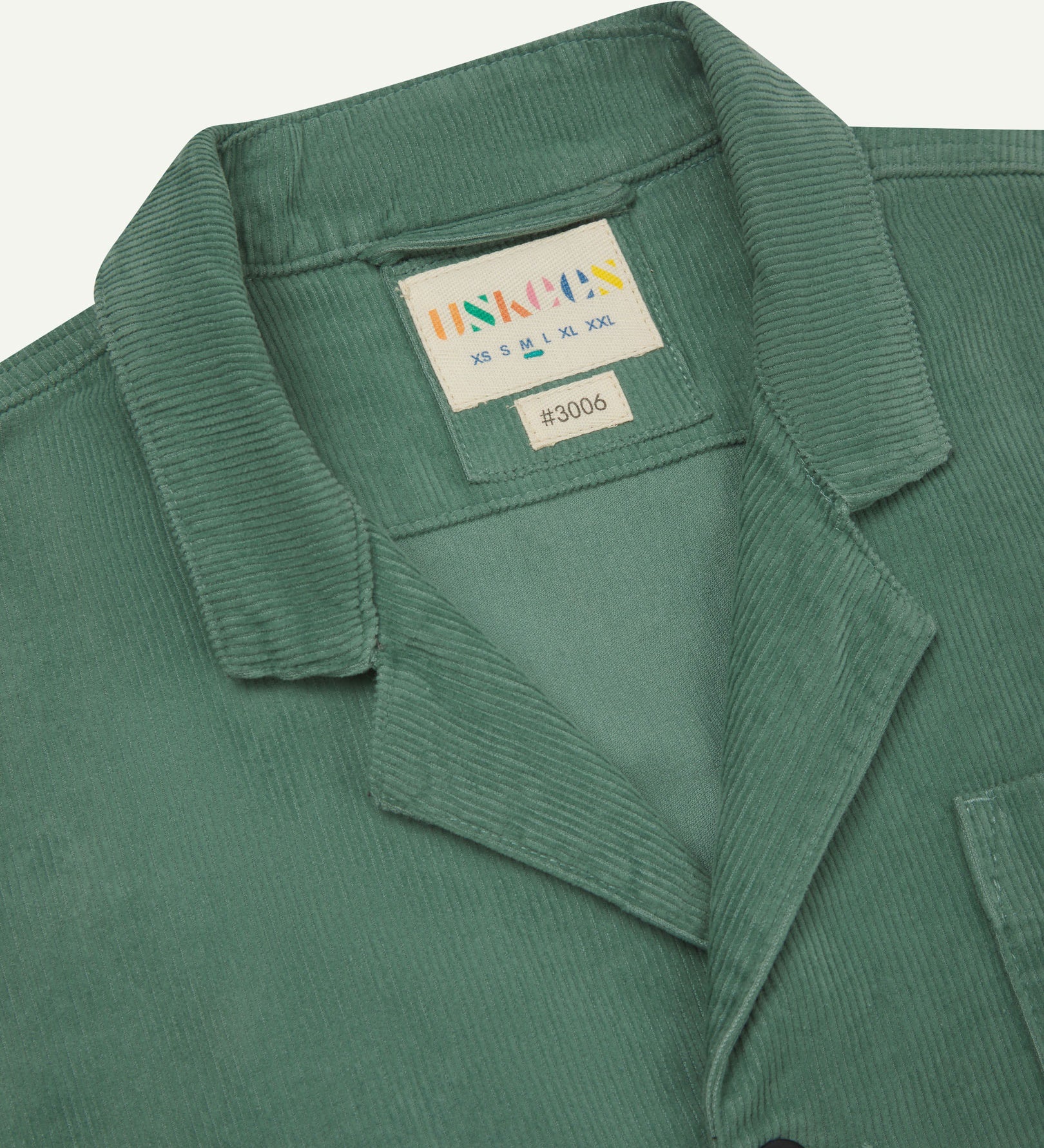 Close-up front view of organic cord eucalyptus-green blazer showing the collar, lapels and Uskees brand label.