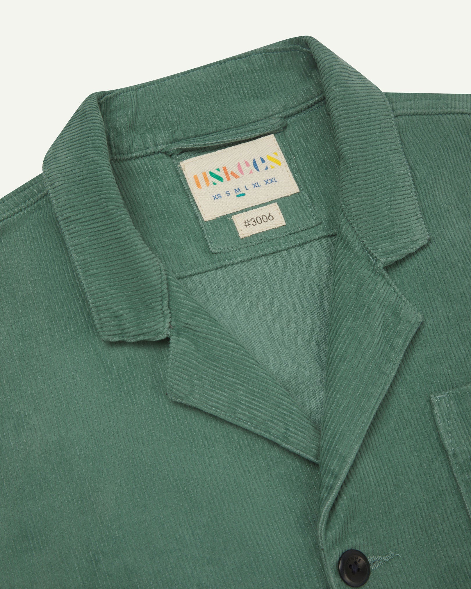 Close-up front view of organic cord eucalyptus-green blazer showing the collar, lapels and Uskees brand label.