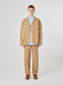 Full-length view of man wearing khaki buttoned organic cotton-twill blazer with clear view of three patch pockets. Paired with matching Uskees pants.