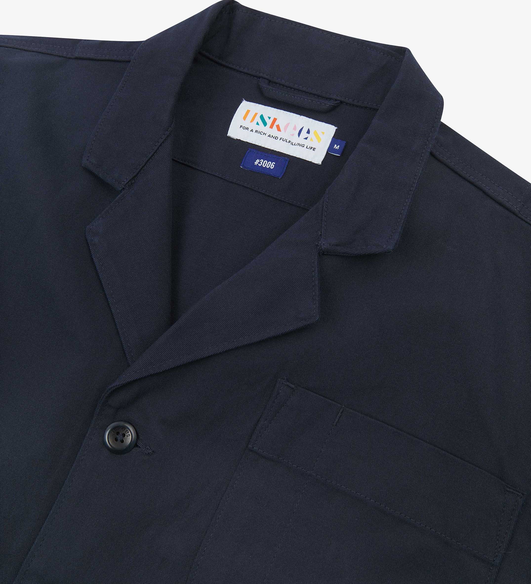 Angled top-half view of #3006, deep blue organic cotton-twill blazer. With focus on collar, lapels, breast pocket, Uskees brand label and corozo buttons.