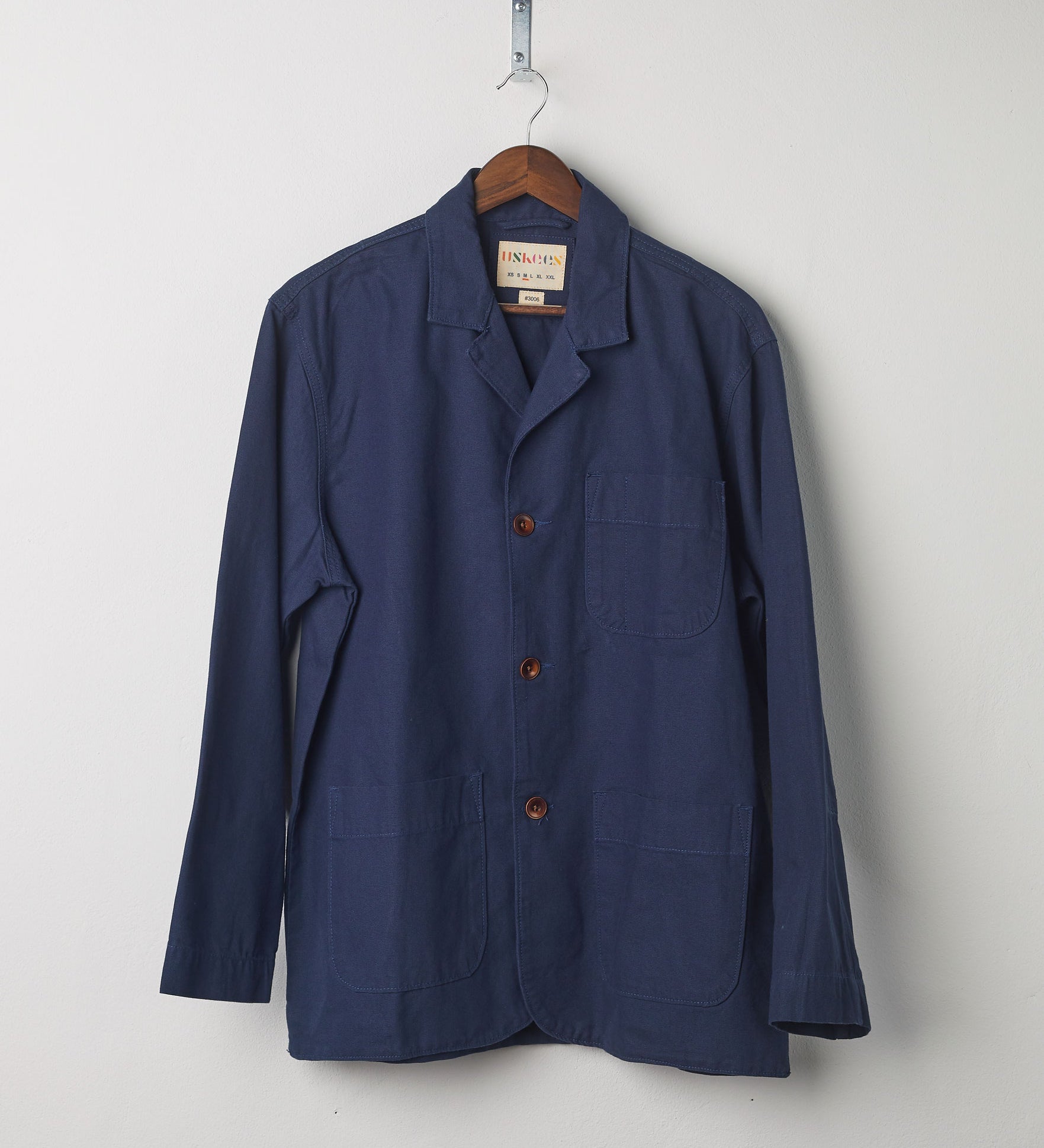 Front view of navy-blue blazer with 3 patch pockets from Uskees, presented on a hanger.