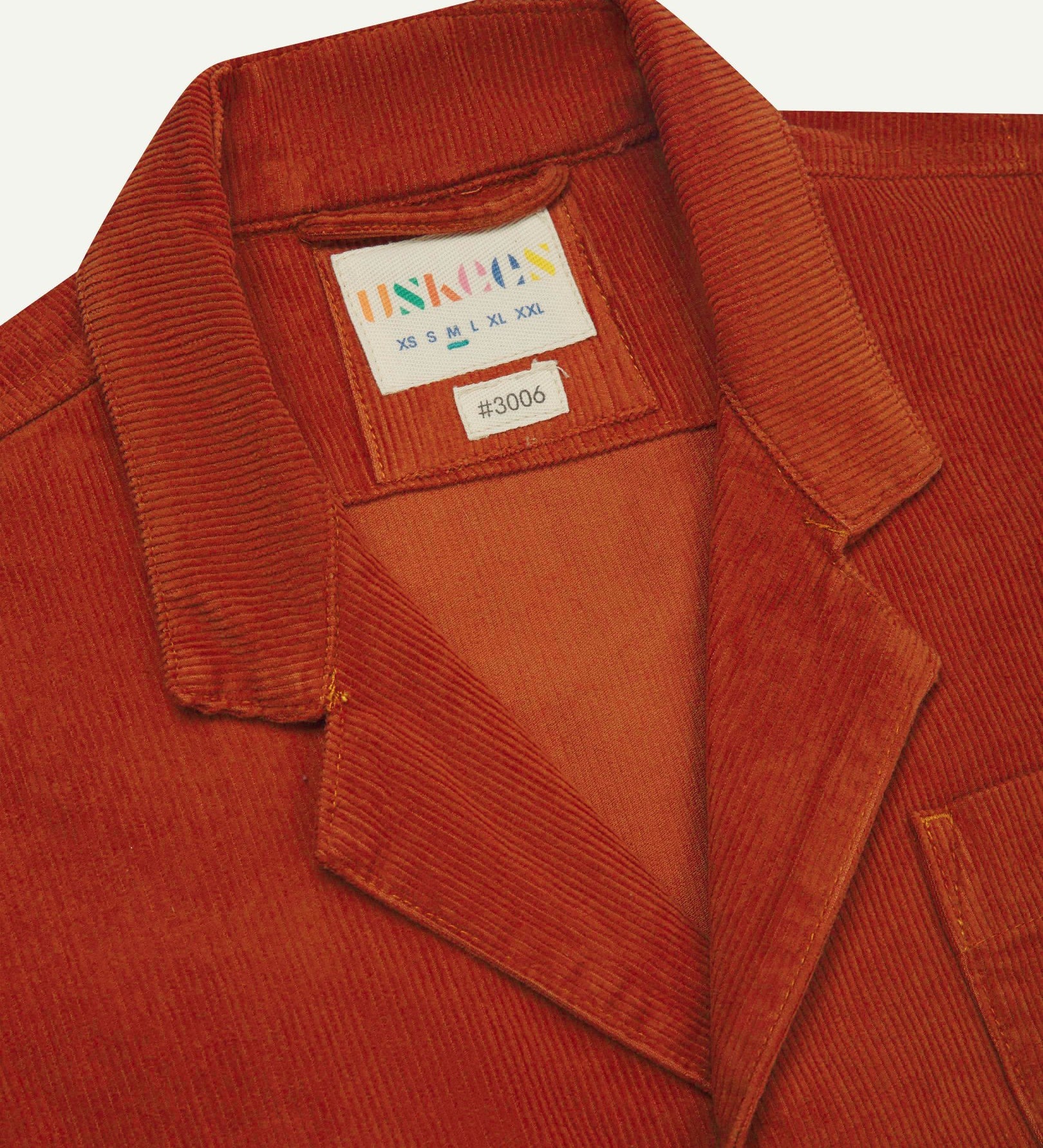 Close-up front view of organic cord rust-red blazer showing the collar, lapels and Uskees brand label.