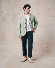 Male model wearing silver-green unbuttoned organic drill blazer from Uskees paired with a white Tee and blue trousers.