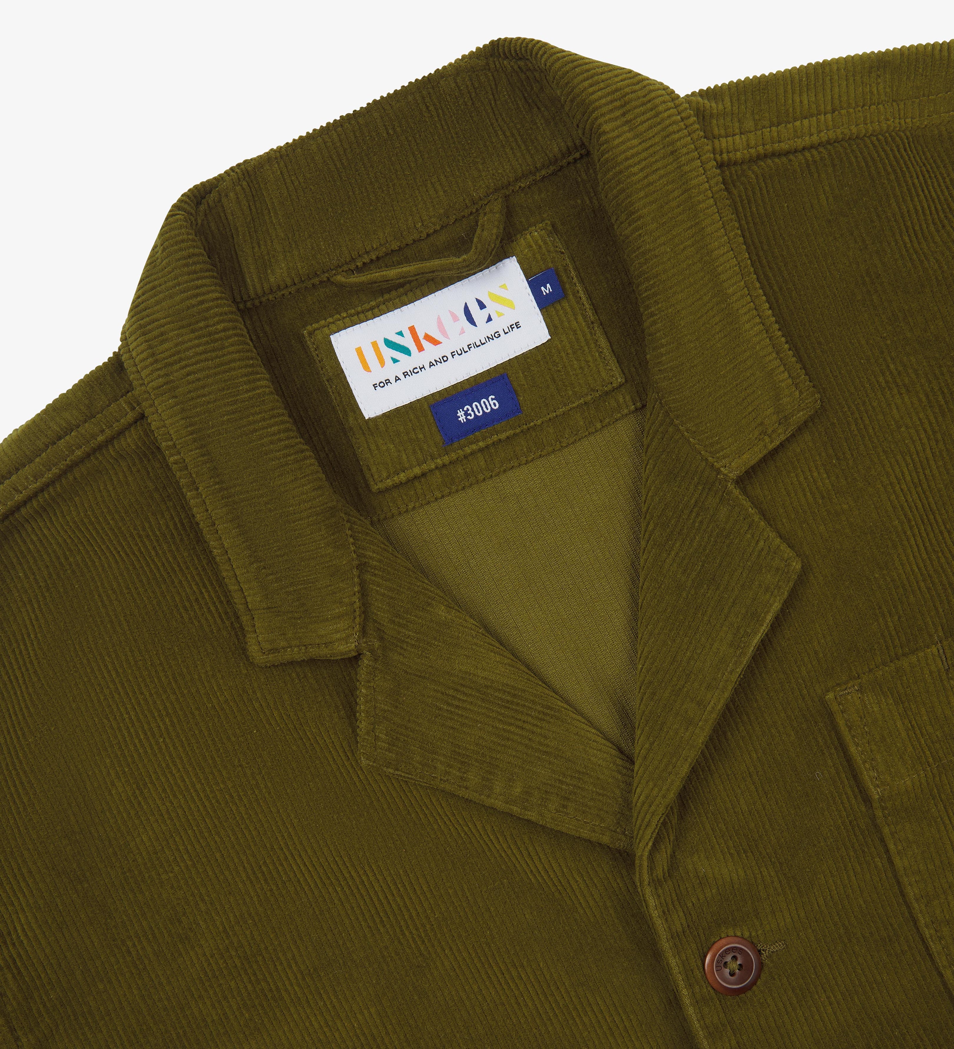 Close-up of an Uskees green corduroy blazer with a brand label on a white background