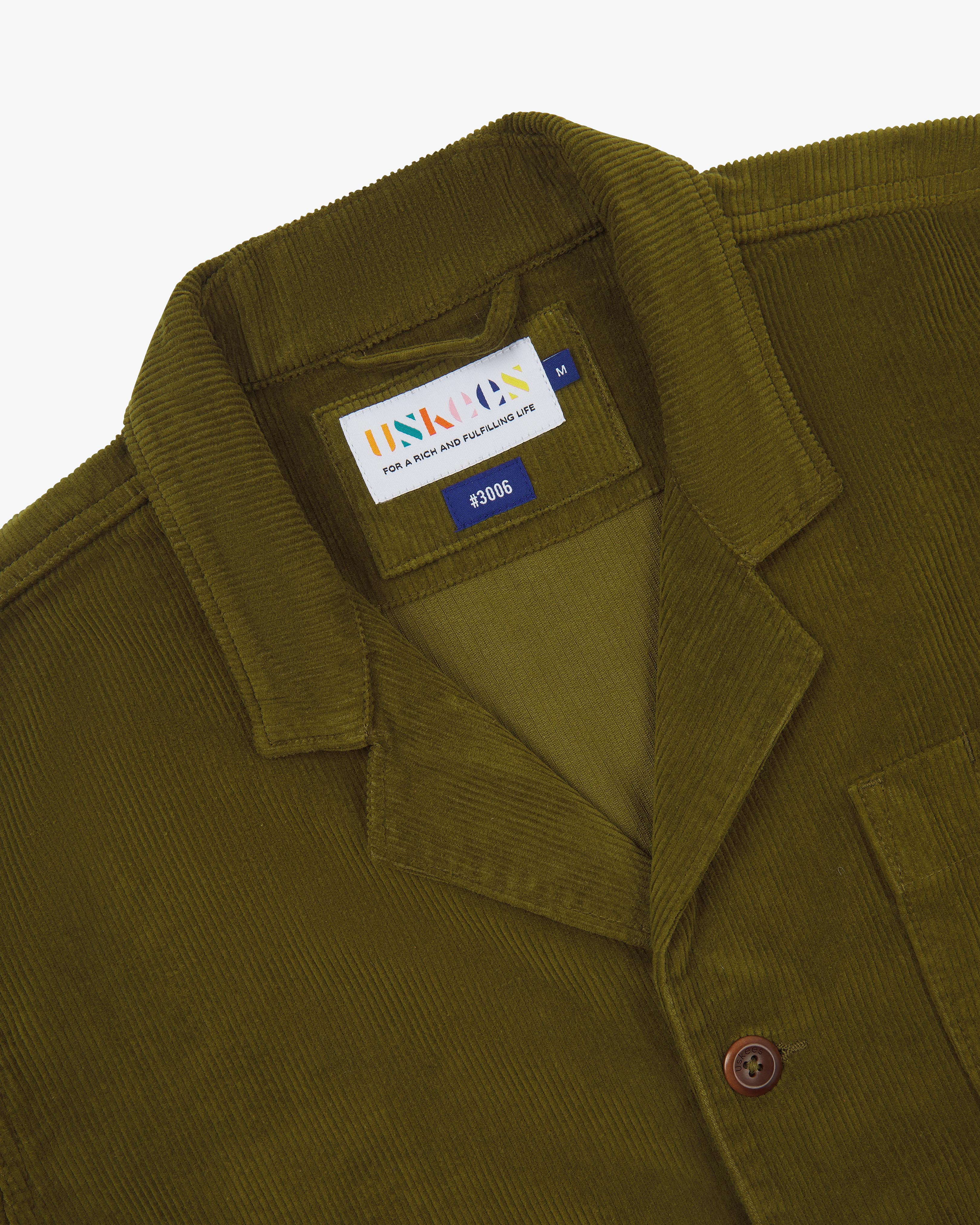 Close-up of an Uskees green corduroy blazer with a brand label on a white background