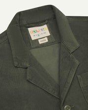 Front close shot of uskees dark green corduroy men's jacket showing collar, lapels and brand/size  label at neck.