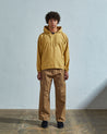 Full-length front view of model wearing Uskees smock in citronella-yellow coloured organic cotton, paired with Uskees tan pants.