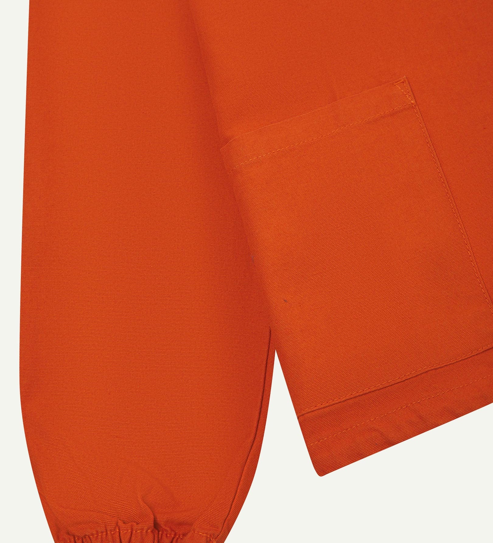 Close front flat shot of Uskees gold-orange organic cotton smock showing ribbed cuff, front pocket and hem.