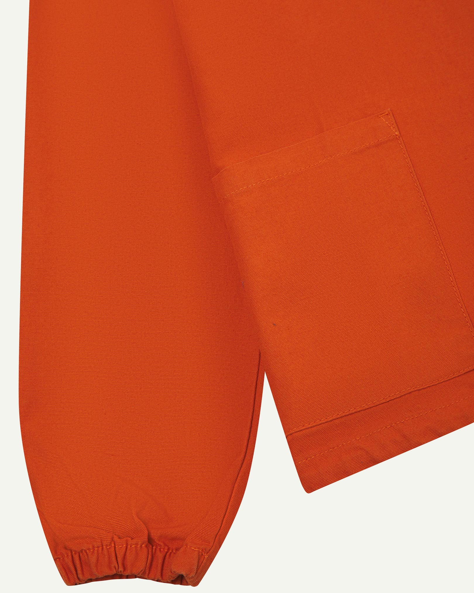 Close front flat shot of Uskees gold-orange organic cotton smock showing ribbed cuff, front pocket and hem.