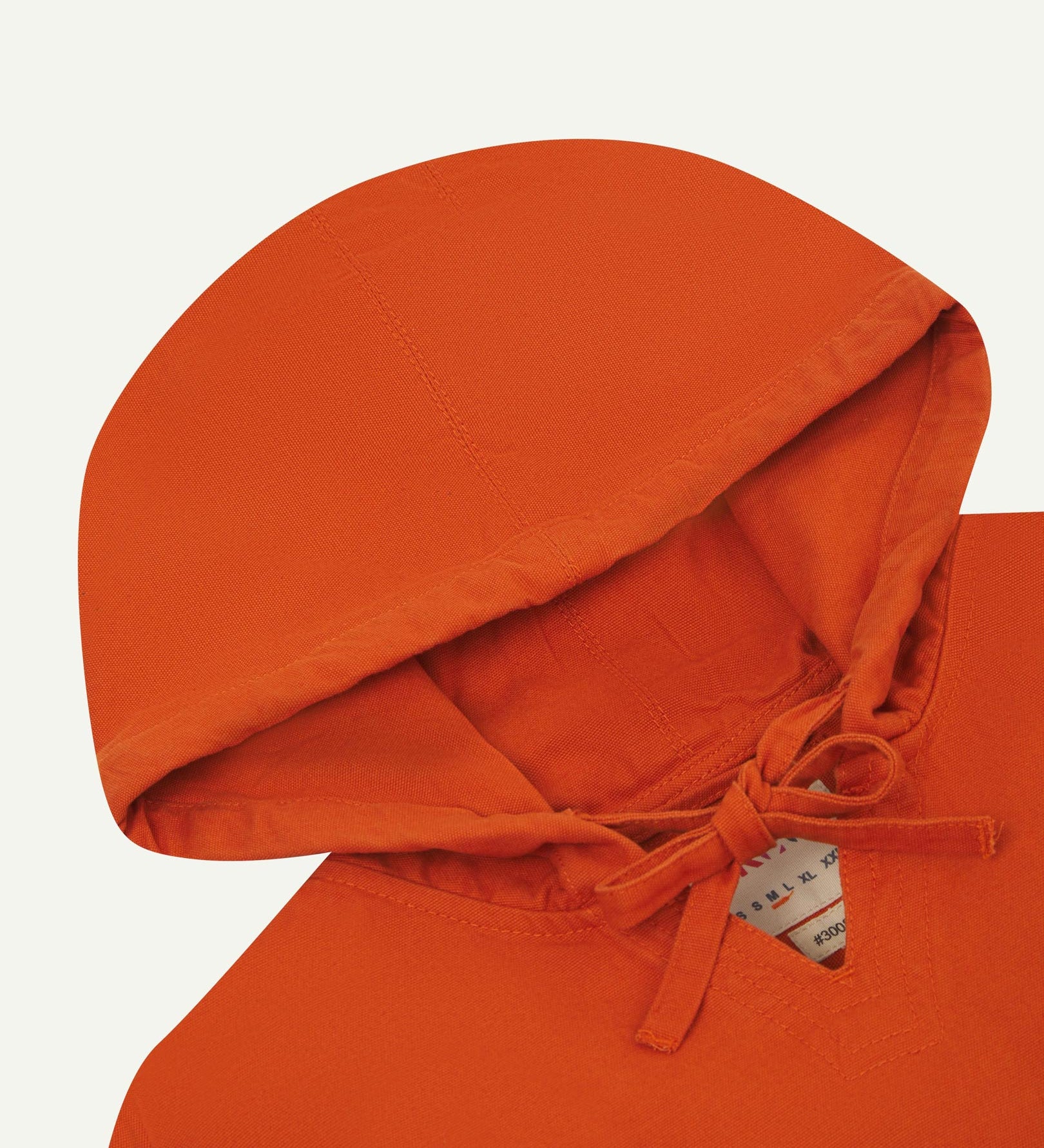 Closer look at the hood of the Uskees organic cotton smock in gold-orange showing hood, hood drawstring and quadruply stitched neck area.