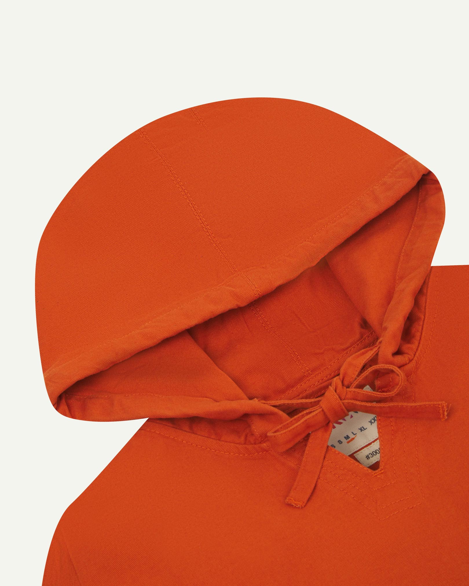 Closer look at the hood of the Uskees organic cotton smock in gold-orange showing hood, hood drawstring and quadruply stitched neck area.