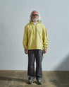 Full-length front of model wearing Uskees Smock in pale yellow organic cotton, paired with loose grey pants.