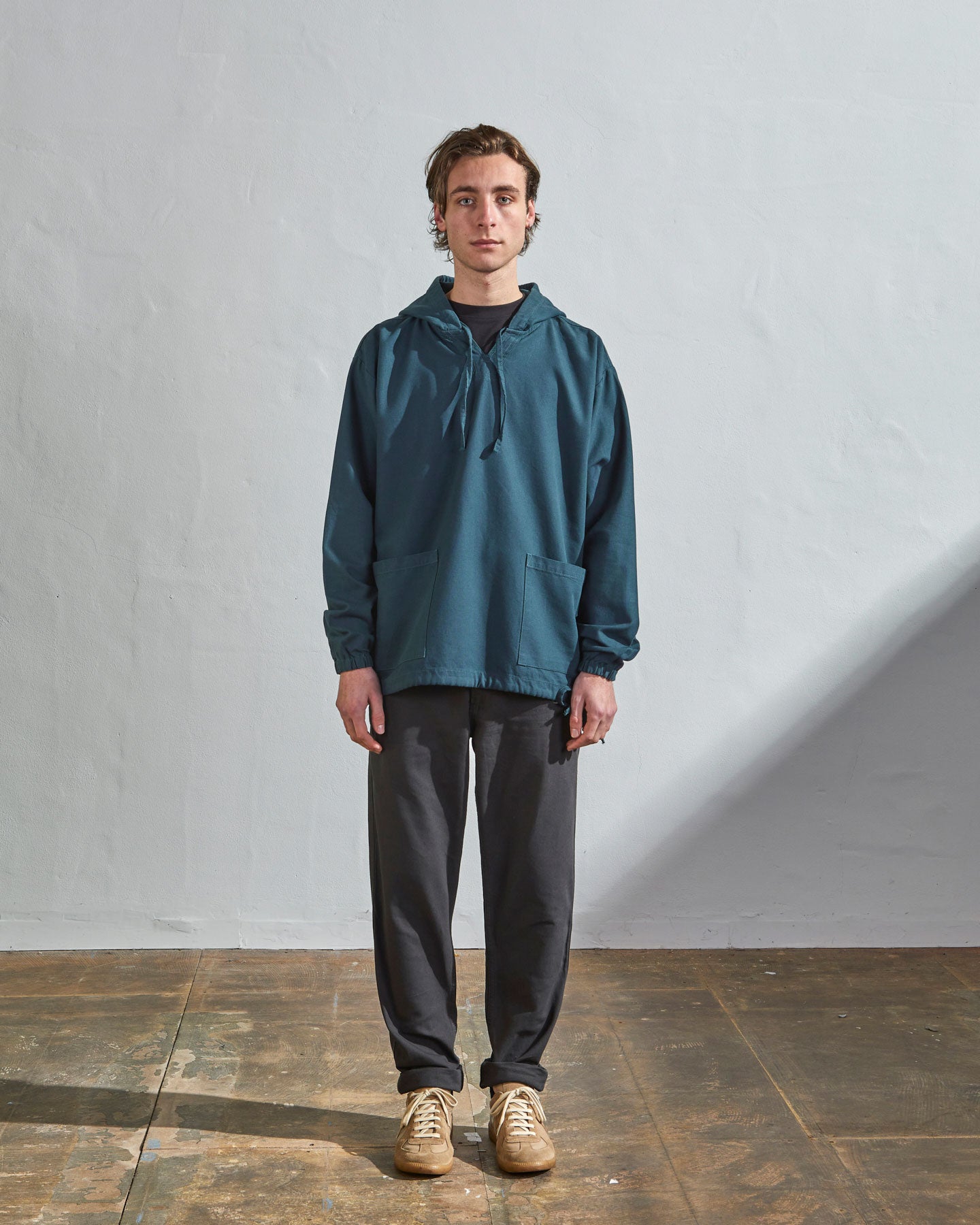 Full-length front view of model wearing Uskees smock in peacock-coloured organic cotton, paired with charcoal-grey pants.