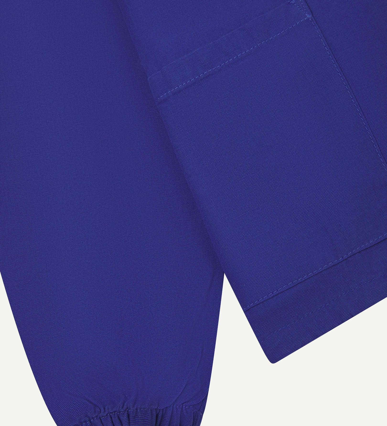 Close front flat shot of Uskees ultra blue organic cotton smock showing ribbed cuff, front pocket and hem.