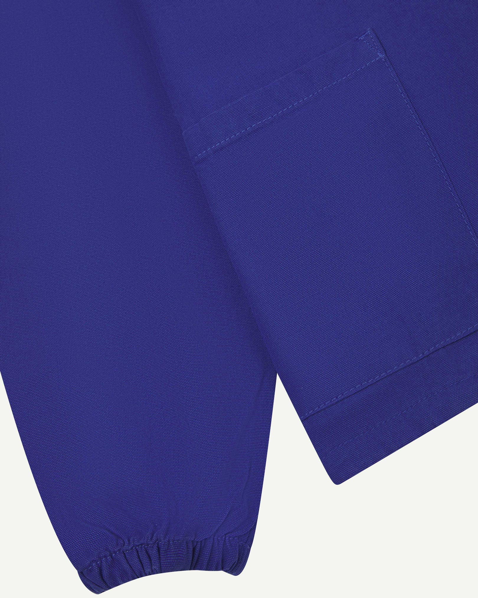 Close front flat shot of Uskees ultra blue organic cotton smock showing ribbed cuff, front pocket and hem.