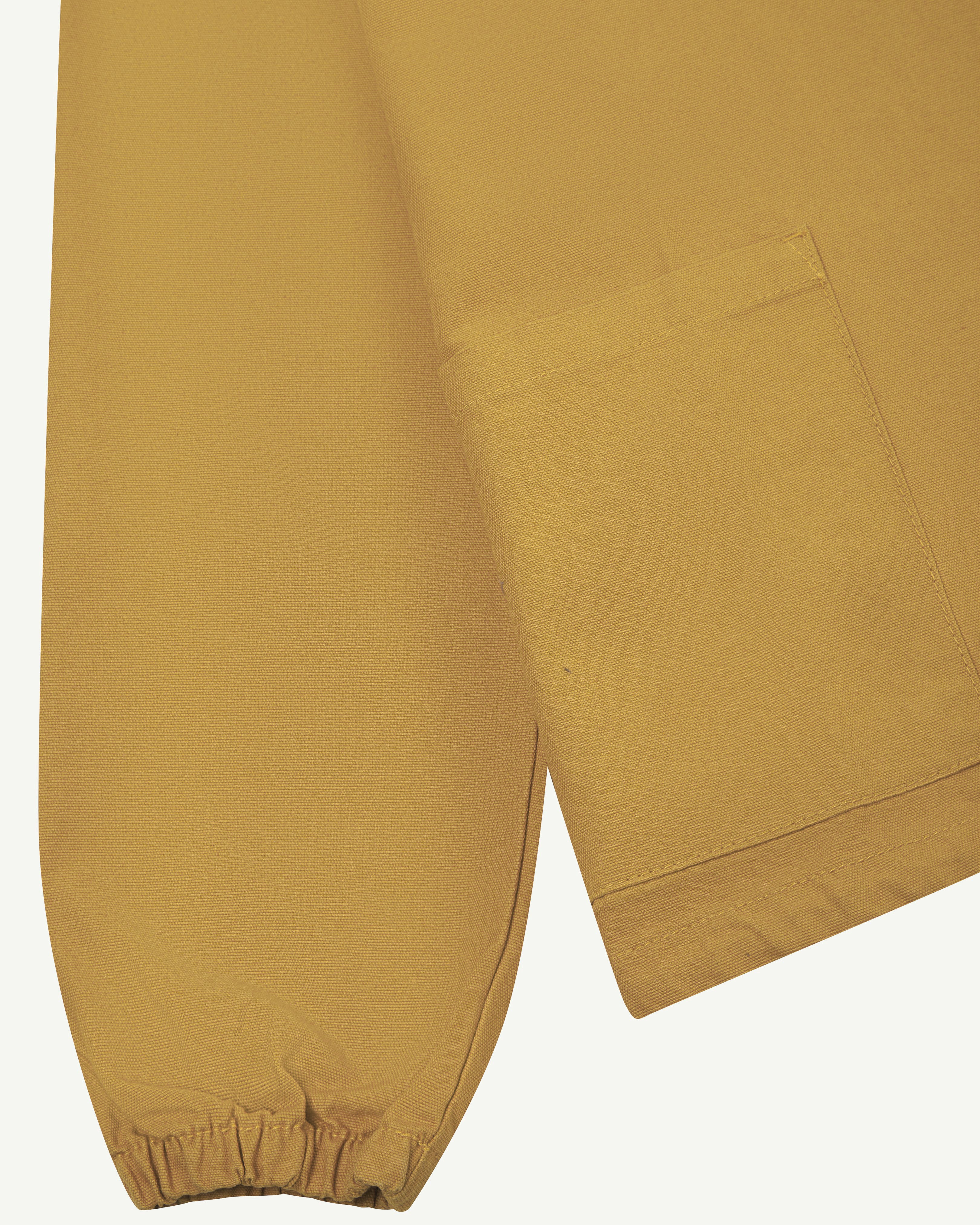 Close-up front flat shot of uskees yellow men's organic cotton smock showing sleeve, elasticated cuff and pocket.