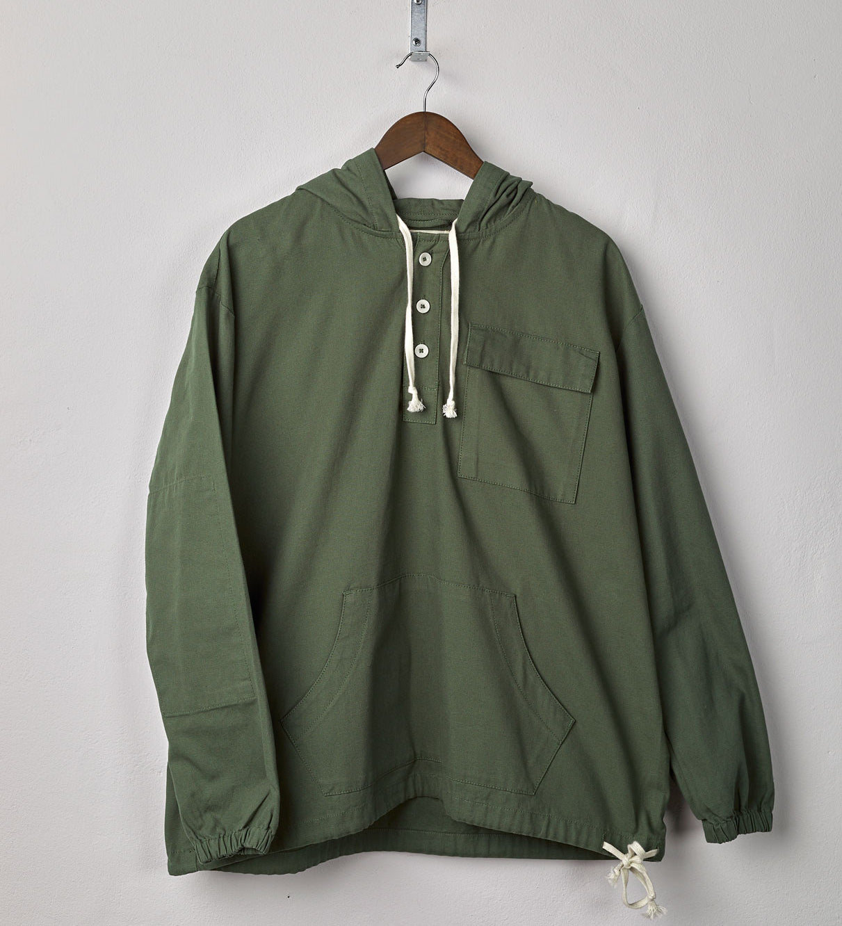 Front view of 'coriander-green' coloured buttoned smock from Uskees with deep front pockets. Presented on hanger.