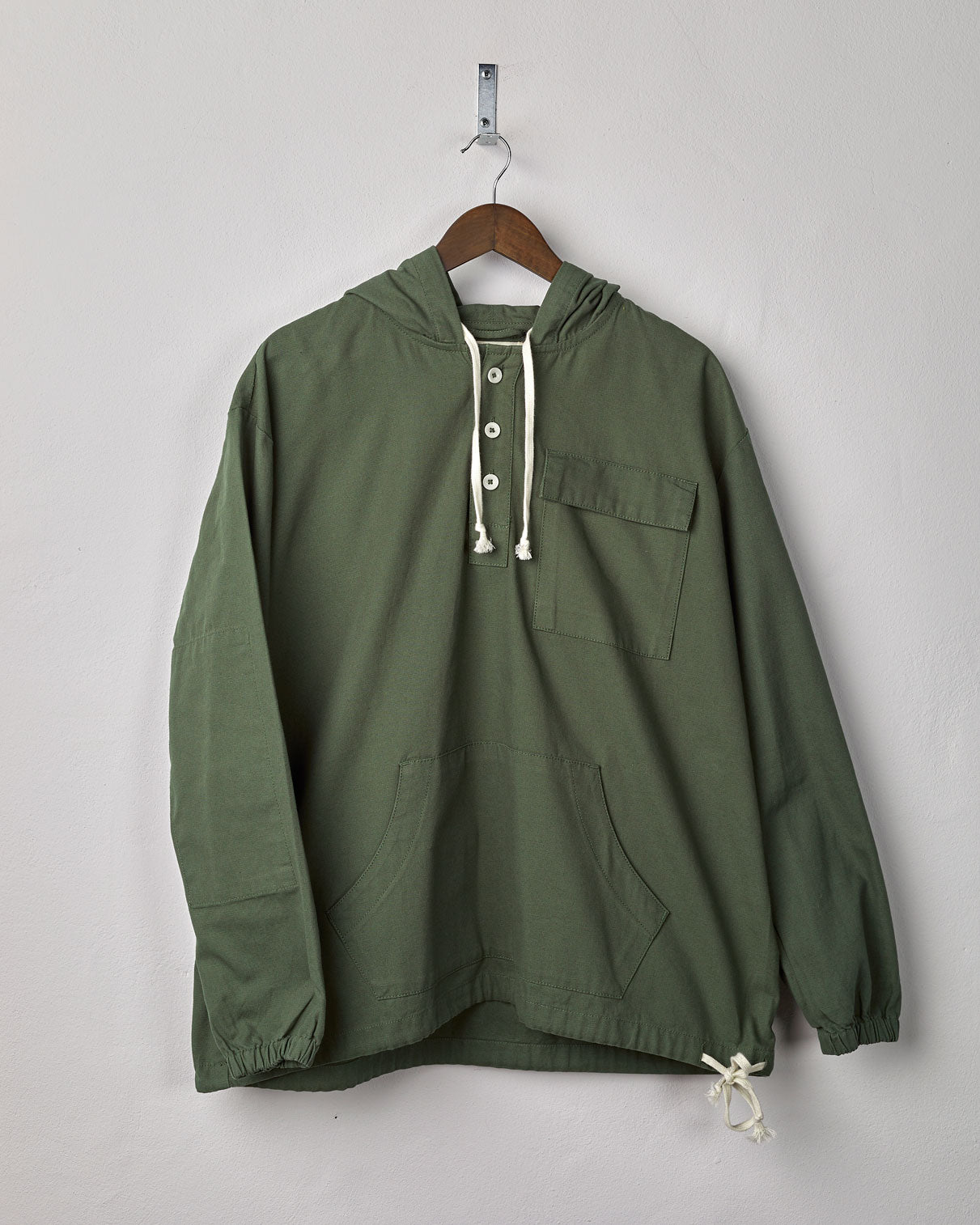 Front view of 'coriander-green' coloured buttoned smock from Uskees with deep front pockets. Presented on hanger.