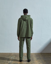 Full-length back view wearing Uskees 'coriander-green' coloured buttoned smock, with view of hood, reinforced elbows and boxy silhouette.
