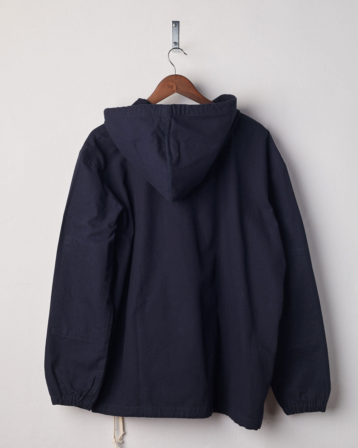 Back view of midnight blue coloured buttoned smock from Uskees with view of hood. Presented on hanger with white backdrop.