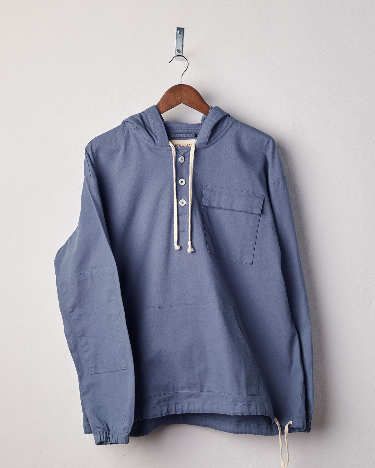 Front view of teal coloured buttoned smock from Uskees with deep front pockets. Presented on hanger with white backdrop.