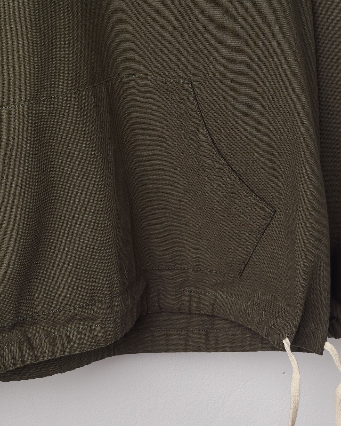Close-up of 'vine green' coloured buttoned smock from Uskees with focus on hemline drawstring and double pocket.