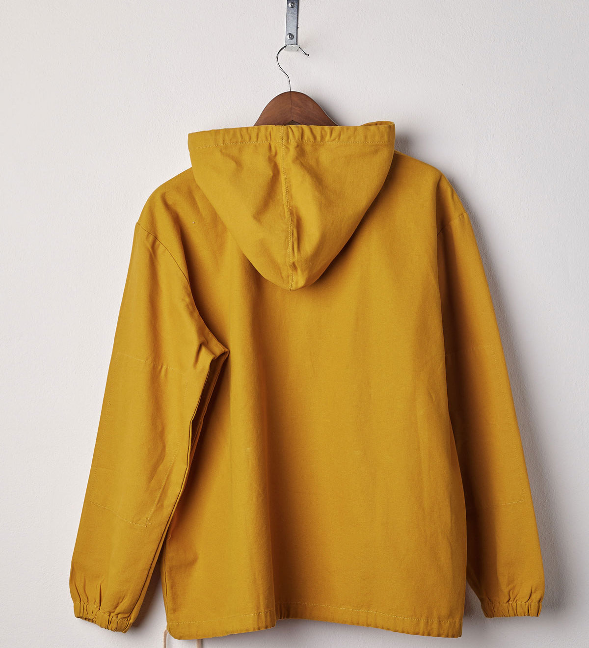 Back view of yellow coloured buttoned smock from Uskees with view of hood. Presented on hanger with white backdrop.