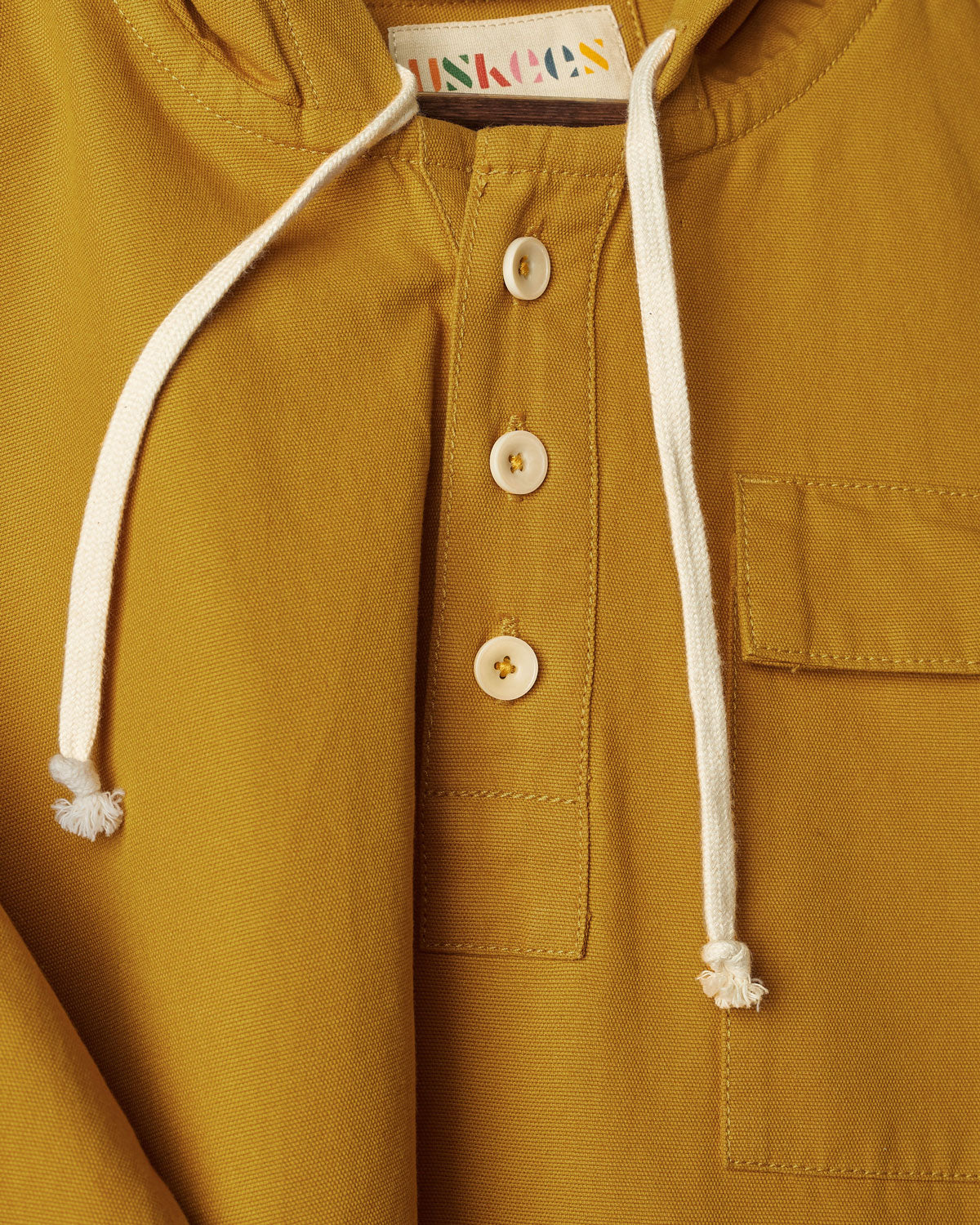 Closer front view of Uskees yellow smock with focus on front buttons, neck drawstring and breast pocket.